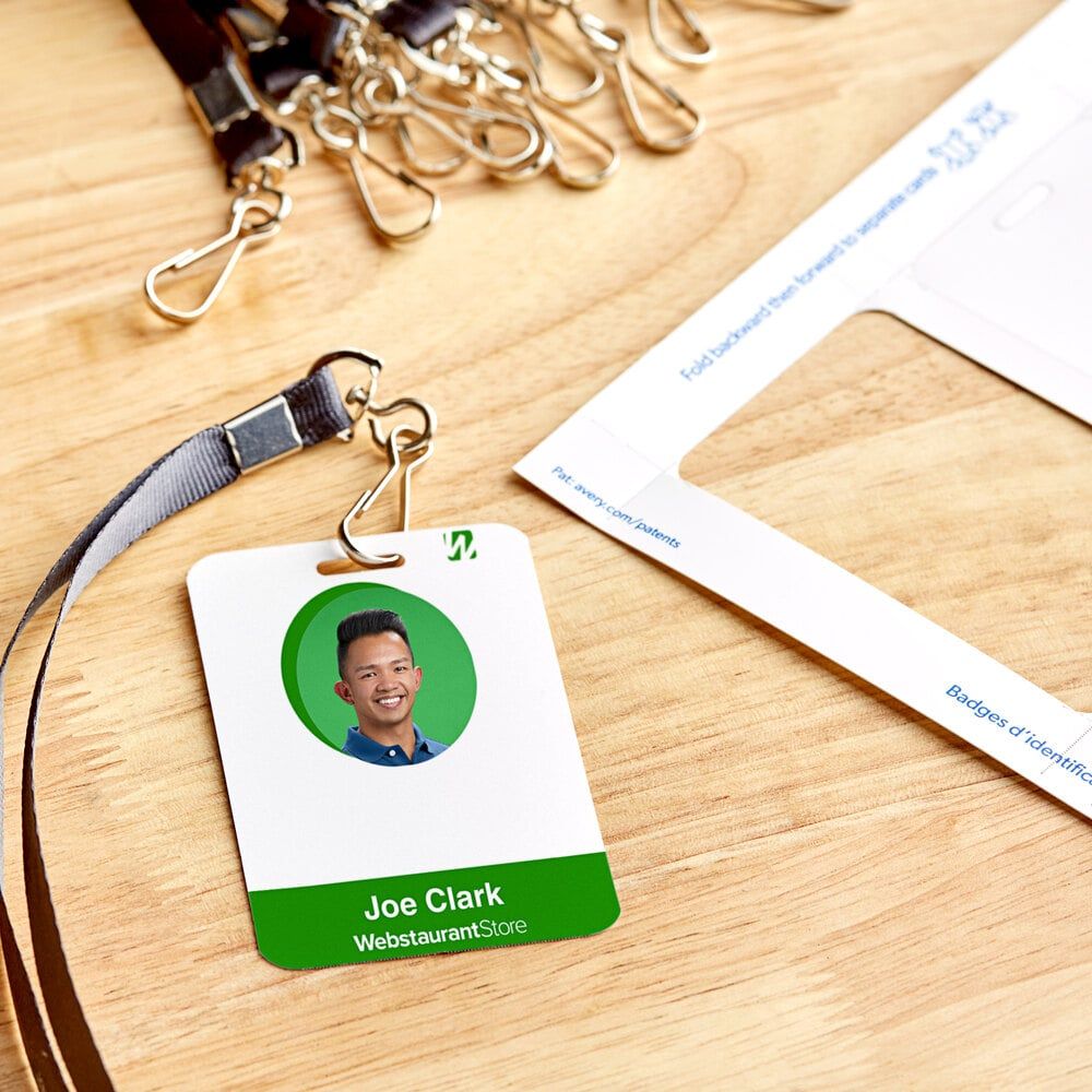 A close-up, top-down shot of several professionally designed employee ID cards laid out on a clean, modern desk. Each card features a distinct company logo, a clear employee photo placeholder, name, title, and subtle security features like a barcode or ho